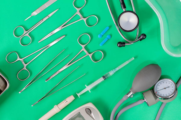 Medical equipment on green surface, including stethoscope, syringe, and thermometer.